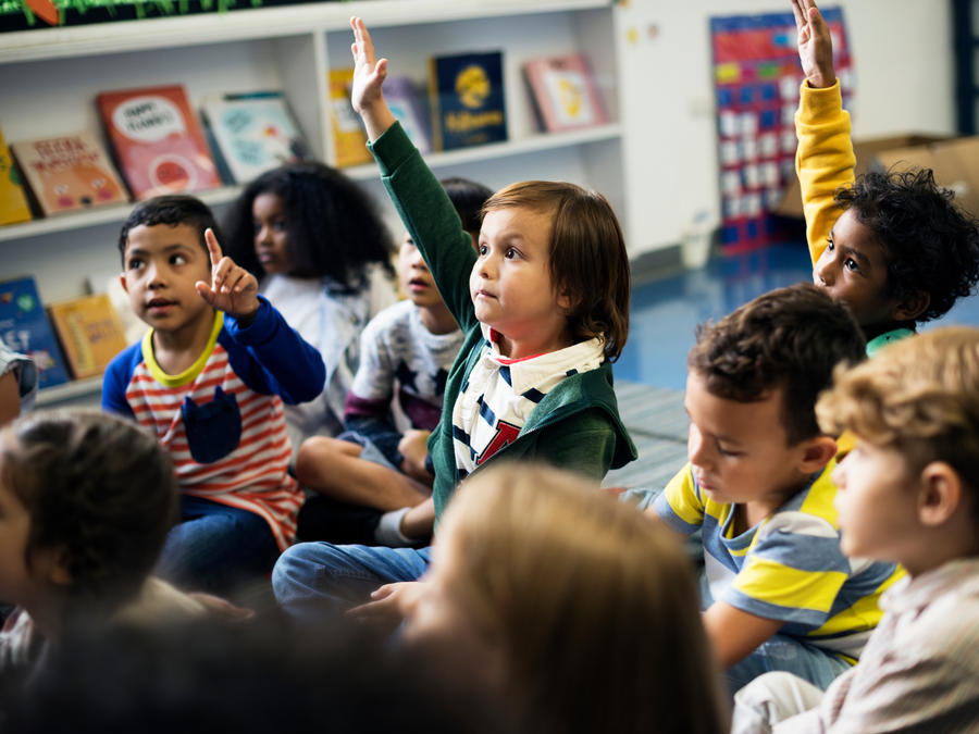 Children raising hands in a classroom.